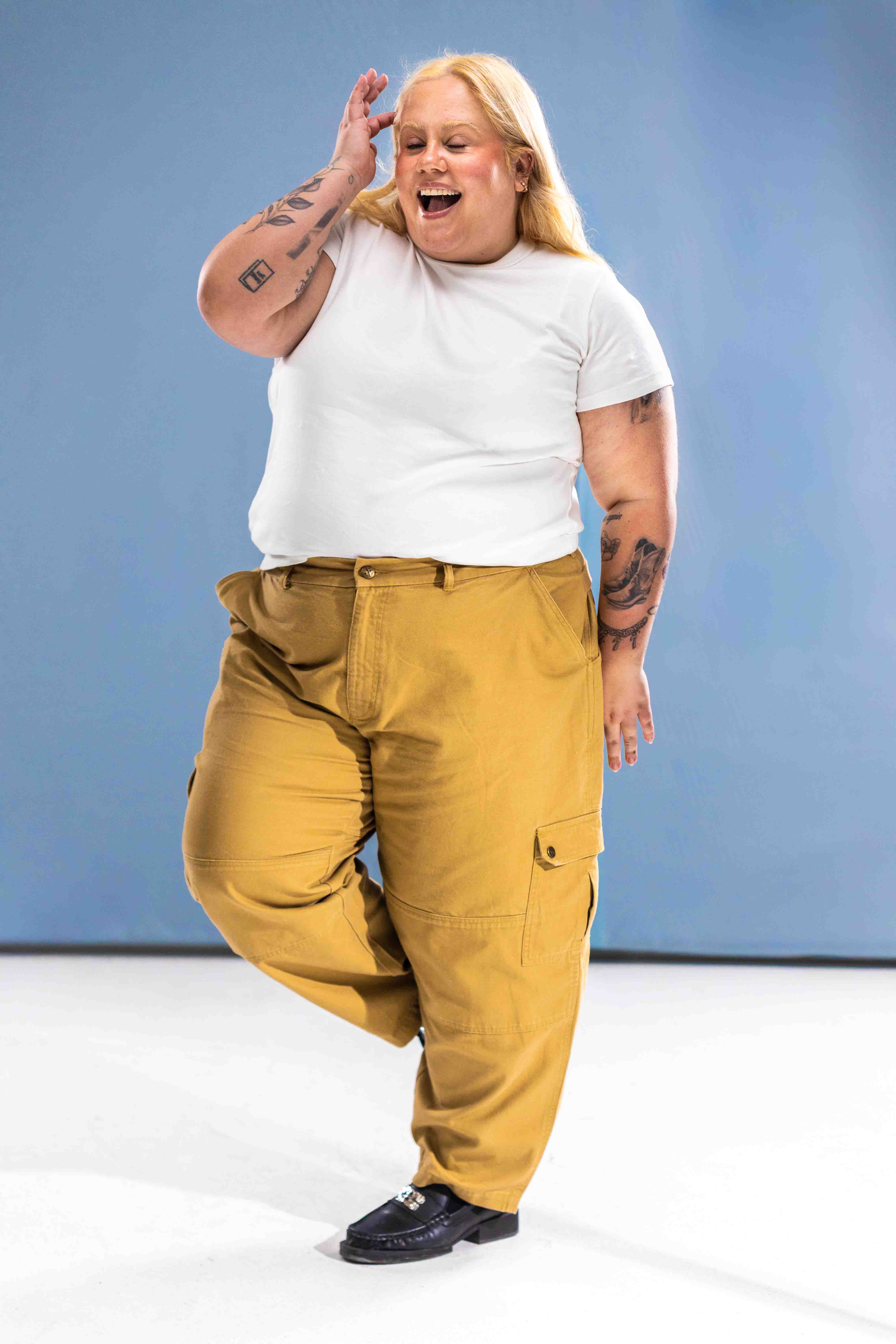 Person wearing a white t-shirt and mustard yellow pants against a blue background